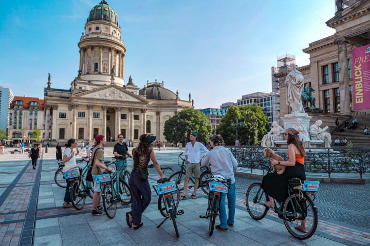 Group of people on rental bikes in a plaza with historic buildings.