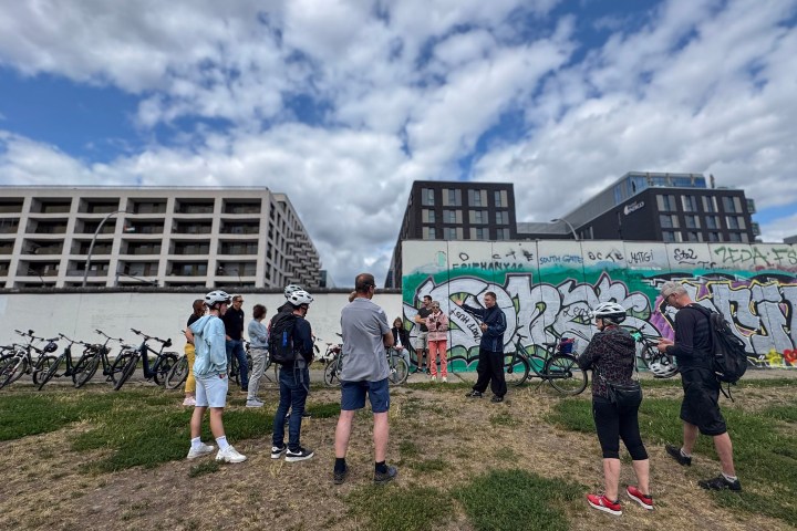 Group of people with bikes standing near a graffiti-covered wall.