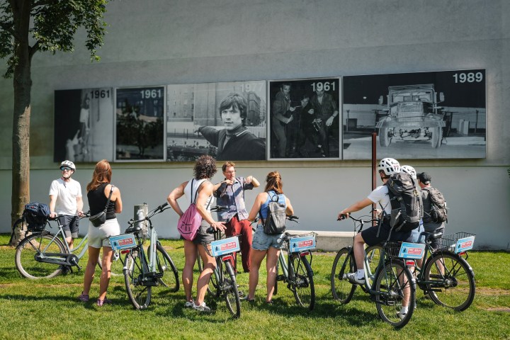 Group of cyclists stopped by a wall with historical photos.