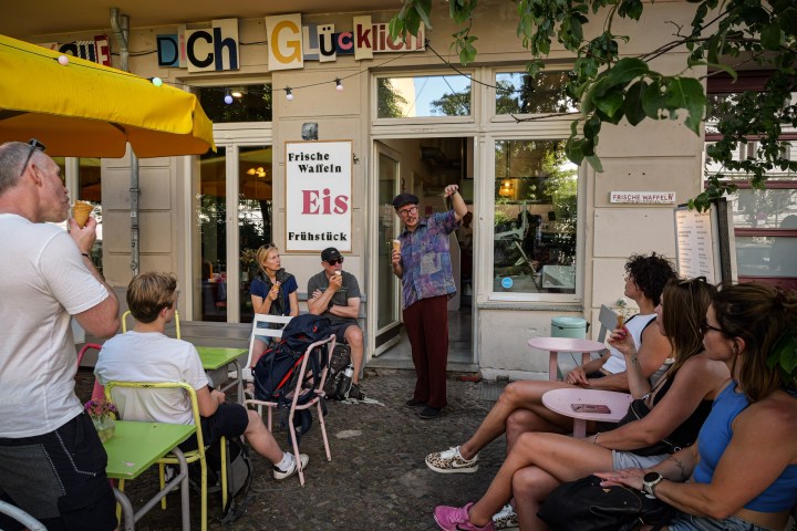 People eating ice cream outside a cafe under a sign with colorful letters.