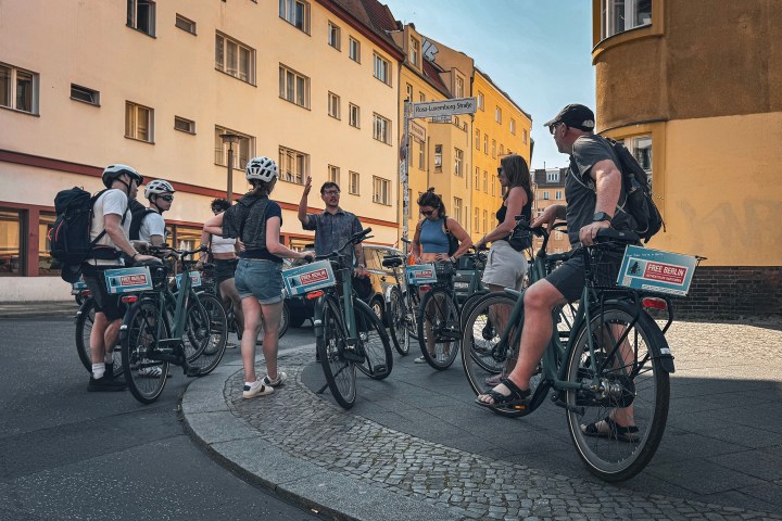 Group of cyclists on a street corner with buildings in the background.