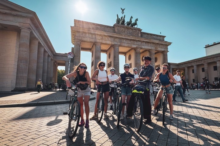 Group of cyclists in front of the Brandenburg Gate on a sunny day.