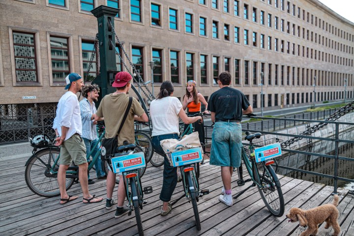 Group of people with bicycles talking on a bridge, a dog walks nearby.