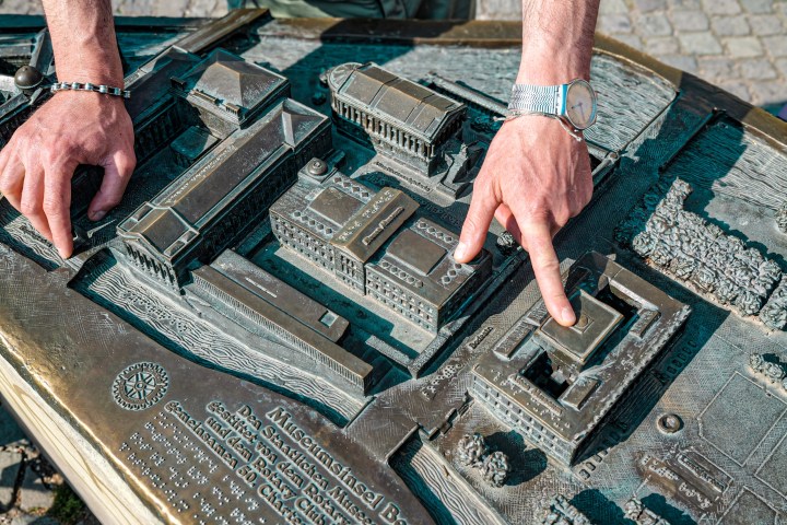 Hands pointing at a detailed bronze 3D model of Berlin buildings.
