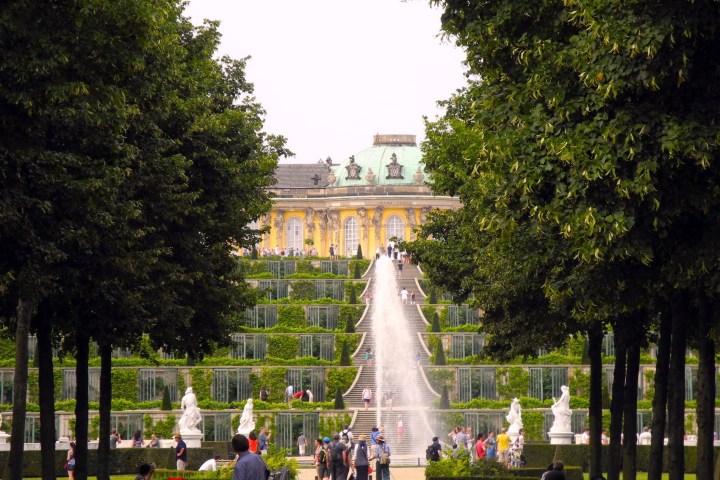 People walking near a grand staircase with a fountain, framed by trees.