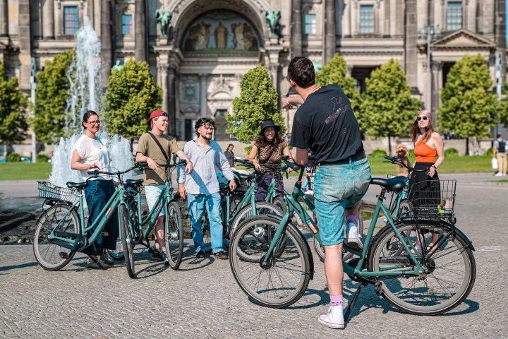 Group of people on bicycles chatting near a fountain in front of a historic building.