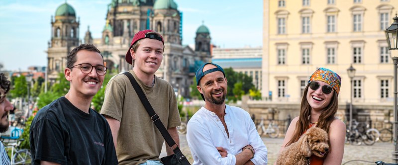 Four people and a dog smiling with Berlin Cathedral in the background.