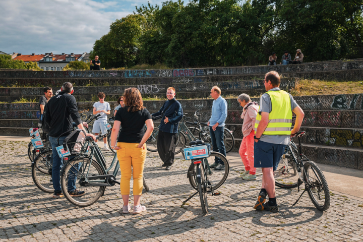 Group of people standing with bicycles in a park or urban setting.