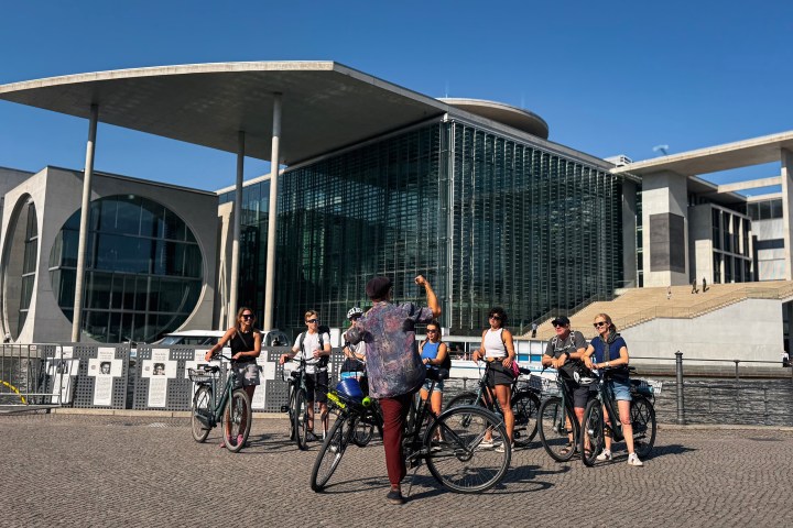 Group of cyclists stopped near a modern building under a clear blue sky.