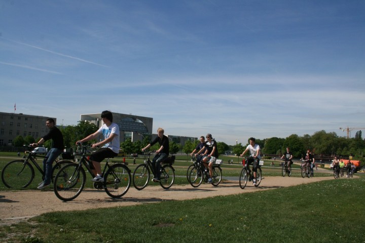 Group of people cycling on a path in a park under a clear blue sky.