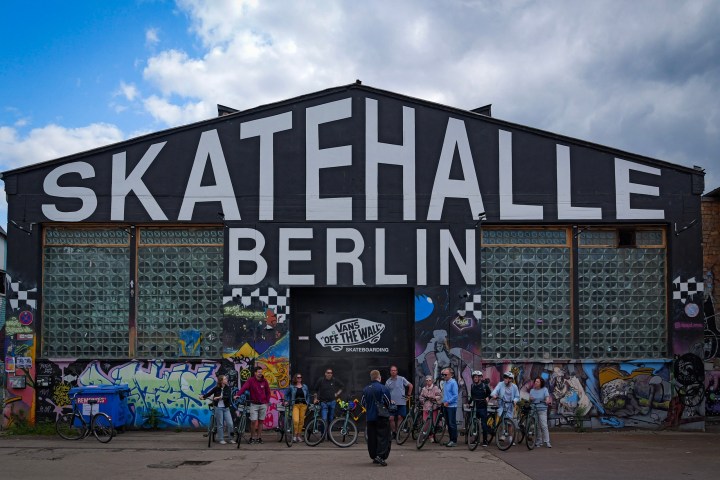 Group of people with bicycles in front of Skatehalle Berlin warehouse with graffiti.