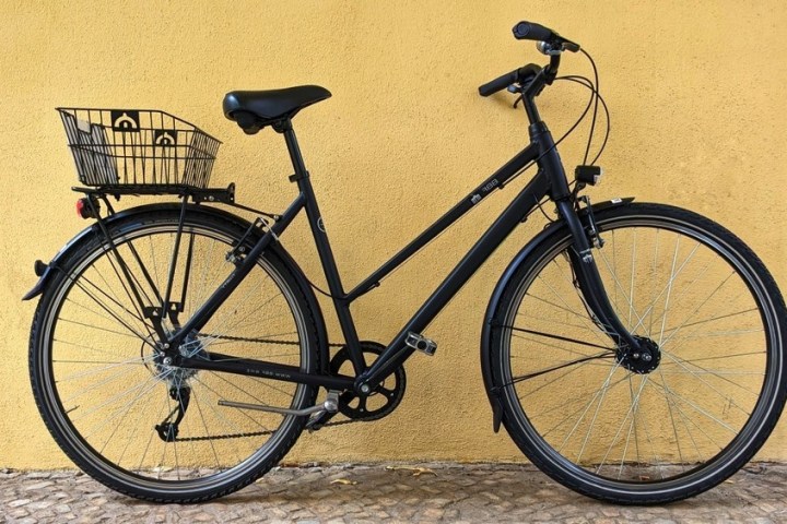 Black bicycle with rear basket against yellow wall.