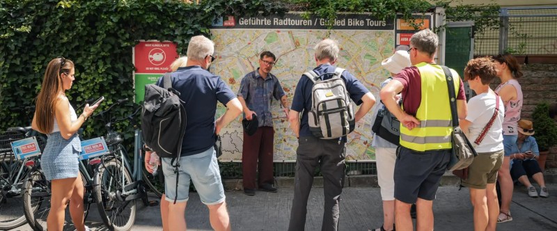 Group of people listening to guide near a map on a sunny street.