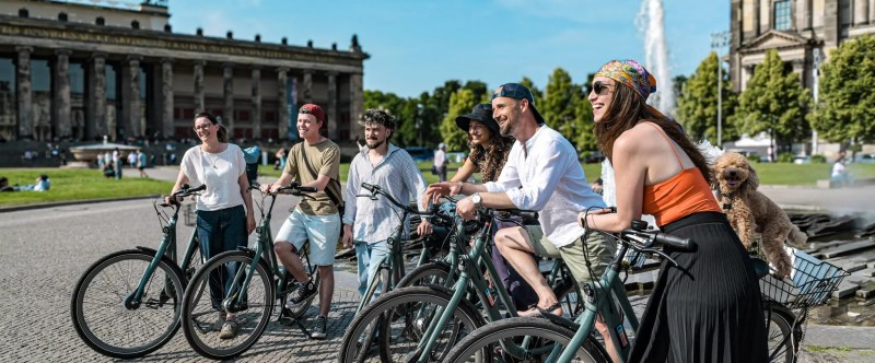 Group of people with bicycles enjoying a sunny day by a historic building.